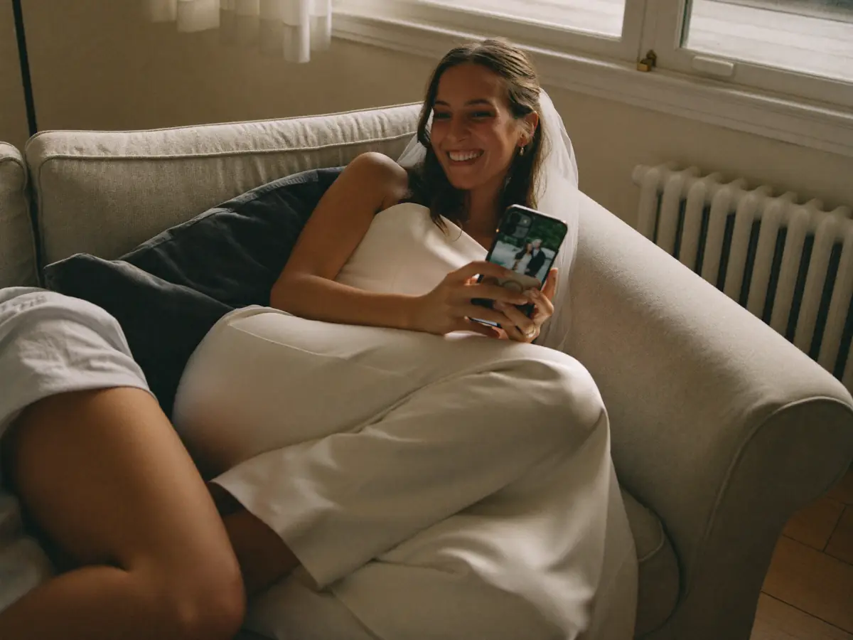 A bride smiling at her wedding photos on her phone