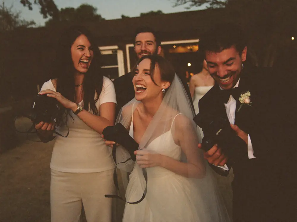 A wedding crew laughing with the bride and groom
